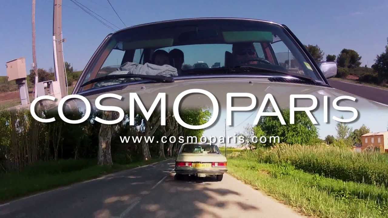 Deux mannequins élégamment vêtus voyagent en voiture vintage, symbolisant un mode de vie sophistiqué et intemporel, dans une ambiance estivale et décontractée.