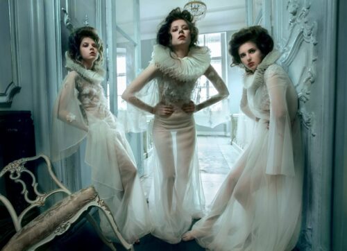 Trois mannequins portent des robes transparentes à col haut et volants, évoquant une esthétique victorienne moderne dans un décor sophistiqué et éthéré.