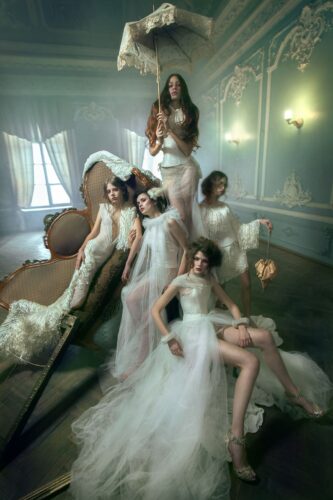 Des mannequins posent dans un salon élégant, vêtus de robes longues en tulle blanc, style haute couture, ambiance romantique et sophistiquée, inspirée de la mode nuptiale contemporaine.