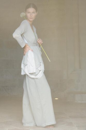 Mannequin portant une tenue longue gris clair au style minimaliste, caractérisée par des lignes épurées et des textures délicates, dans un environnement tamisé évoquant l'élégance contemporaine.