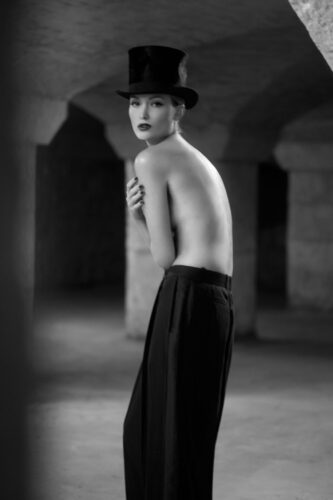 Mannequin en pantalon ample noir et chapeau, torse nu, pose élégante dans une ambiance artistique en noir et blanc, évoquant une esthétique sophistiquée et minimaliste.
