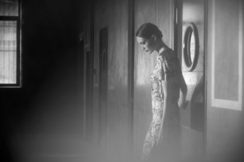Mannequin vêtu d’une robe imprimée, capturé en noir et blanc, dégageant une élégance sobre et intemporelle dans une ambiance mystérieuse et tamisée.