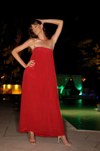 Mannequin en robe longue bustier rouge, pose élégante, ambiance nocturne chic près d'une piscine éclairée, mettant en valeur le style glamour et sophistiqué de la tenue.