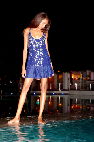 Mannequin portant une robe courte bleue ornée de sequins, silhouette élégante dans un cadre nocturne urbain, style chic et tendance adapté aux soirées estivales sophistiquées.