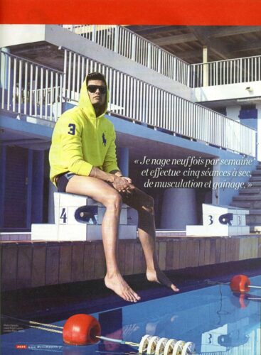 Mannequin posant près d’une piscine, portant un sweat à capuche jaune fluo et un short bleu marine, look sportif et urbain, accessoirisé de lunettes de soleil.