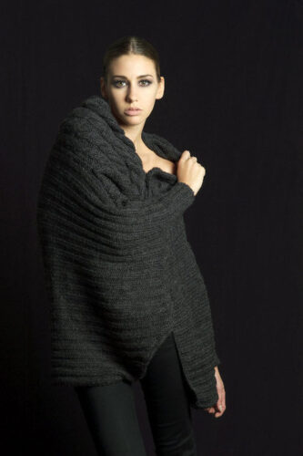 Mannequin portant un manteau oversize en maille grise, style minimaliste et contemporain, sur fond noir, mettant en avant l’élégance et la sophistication hivernale.