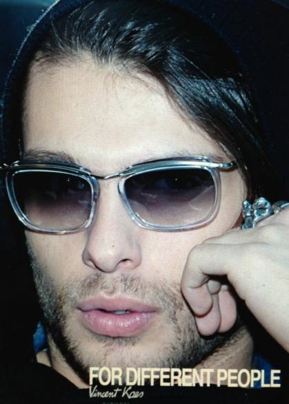 Mannequin masculin portant des lunettes de soleil tendance, barbe de trois jours, cheveux foncés et bague argentée, incarnant un style urbain sophistiqué.