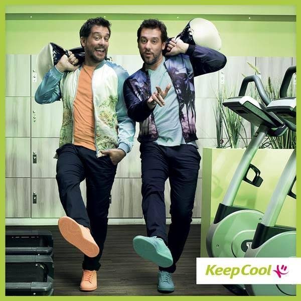 Deux mannequins portent des tenues sportives colorées et décontractées, associant vestes imprimées et pantalons sombres, posant avec confiance dans une salle de sport contemporaine.