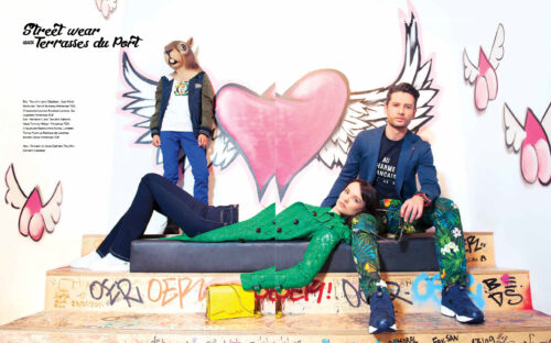 Trois mannequins posent devant un graffiti coloré, vêtus de tenues urbaines tendances aux motifs audacieux, avec accessoires modernes, capturant l’esprit contemporain de la mode streetwear.