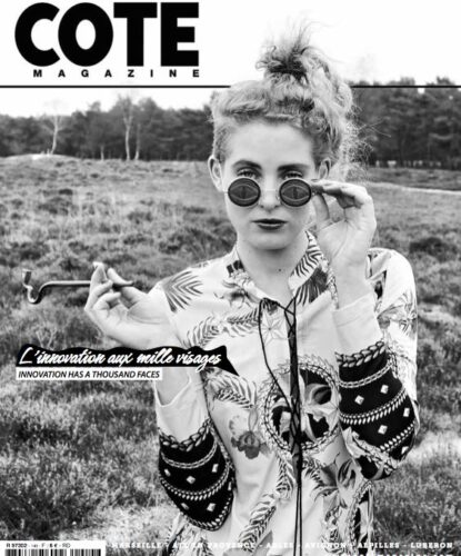 Mannequin en chemise imprimée baroque, lunettes rondes rétro, coiffure relevée, pose assurée en extérieur, incarnant une esthétique vintage et avant-gardiste pour une couverture de magazine de mode.