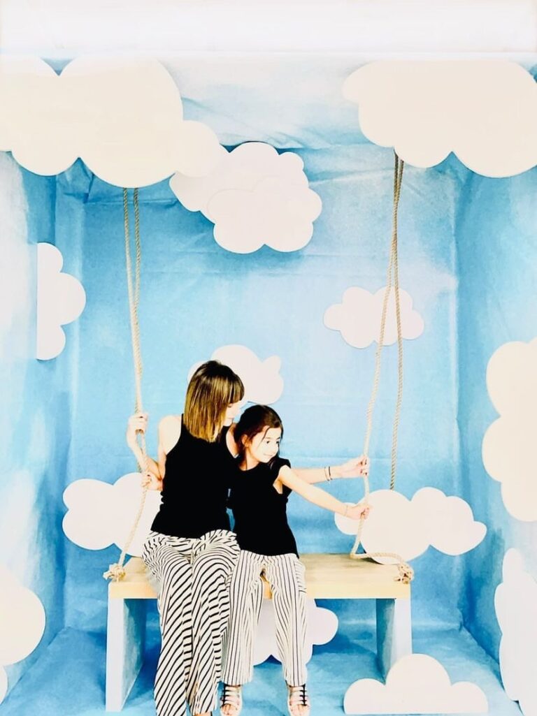 Installation scénographique représentant un ciel bleu avec des nuages en papier et une balançoire, évoquant un décor onirique et poétique pour une vitrine ou une exposition.
