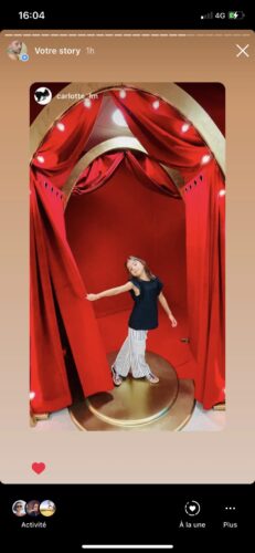 Une installation scénographique sophistiquée avec de lourds rideaux rouges ouverts, dévoilant une figure centrale, imitant une scène de théâtre dans une vitrine élégante.