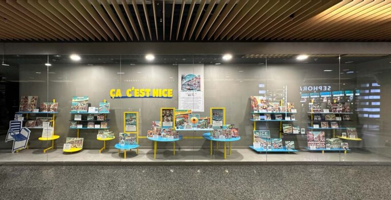 Vitrine élégante mettant en avant des livres et objets, agencés sur des présentoirs colorés, style moderne et épuré, sans mannequins visibles, ambiance contemporaine et soignée.