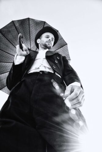 Mannequin homme vêtu d’un costume élégant noir et blanc, tenant un parapluie, photographié en contreplongée; style rétro et raffiné, ambiance sophistiquée.