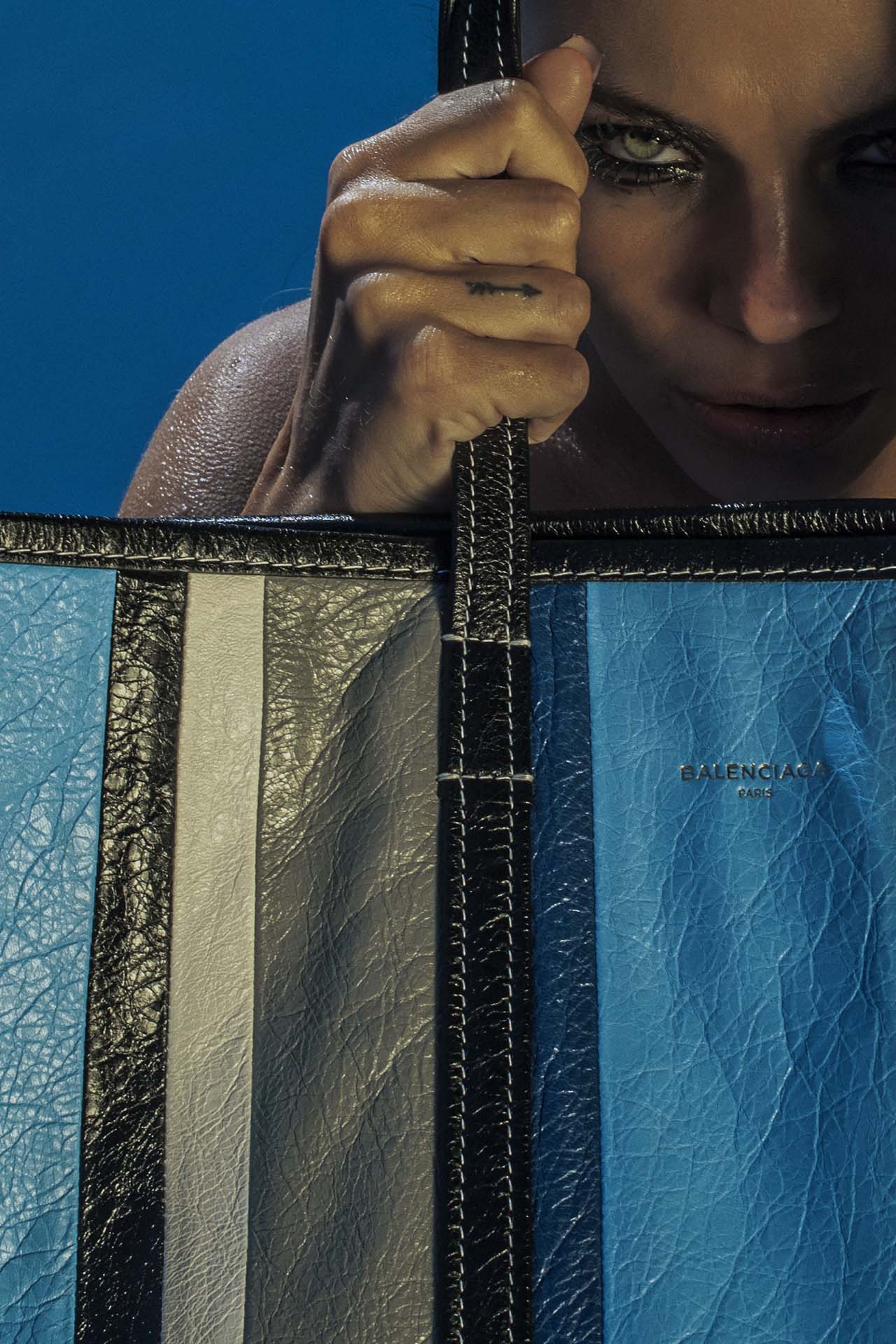 Mannequin tenant un sac de créateur en patchwork bleu et gris, sous une lumière sophistiquée, évoquant une esthétique avant-gardiste et contemporaine.