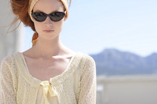 Mannequin portant des lunettes de soleil noires, un bandeau beige et un cardigan en maille crème, posant dans un décor extérieur lumineux.