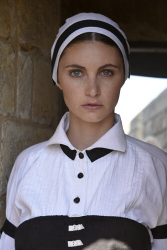 Mannequin portant une chemise blanche élégante à col structuré et détails noirs, accessoirisée d’un bandeau assorti, dans un style épuré et sophistiqué.