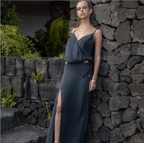 Femme élégante portant une robe Maison Monzerian chic, posant devant un mur de pierre, mettant en valeur la mode haut de gamme et le style raffiné de la marque.