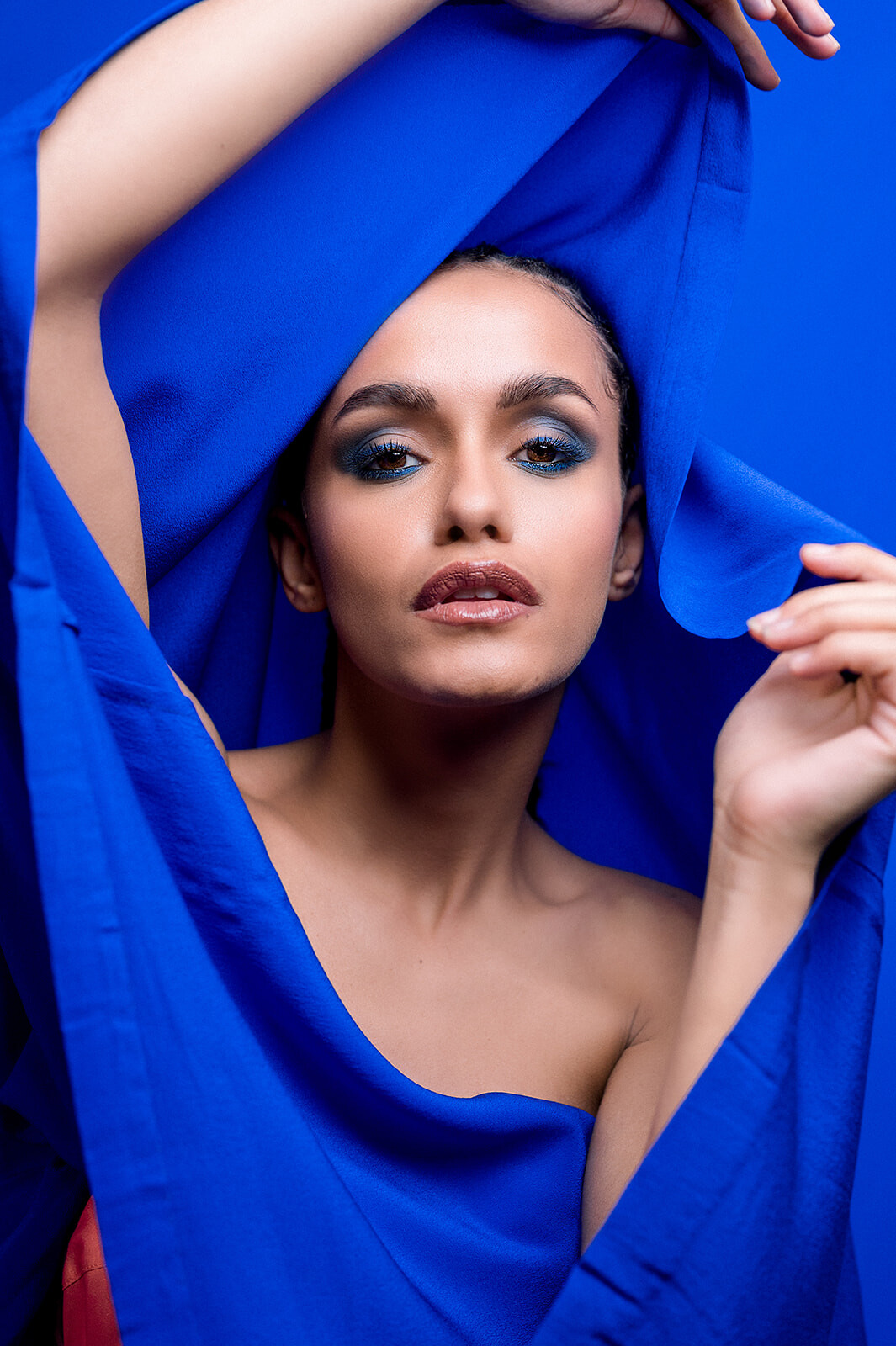 Mannequin posant avec assurance, drapée dans un tissu bleu vif, maquillage sophistiqué aux tons bleus, regard intense, mise en scène élégante et contemporaine.