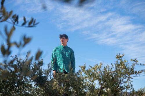 mannequin porte une chemise verte élégante, posé au milieu de la nature, créant un contraste chic entre urbanité et environnement naturel.