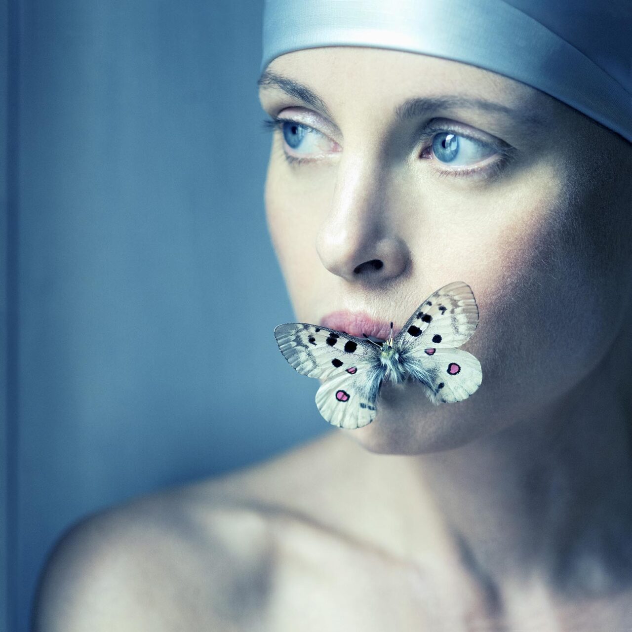 Mannequin au style avant-gardiste, portant un bandeau argenté et une papillon délicate posée sur les lèvres, créant une esthétique énigmatique et artistique dans des tons froids.