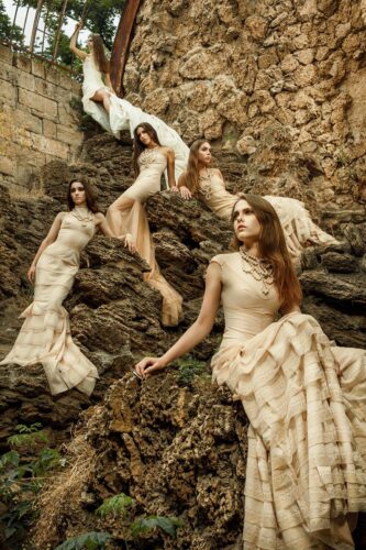 Des mannequins posent en robes longues et élégantes couleur chair sur des rochers, créant une ambiance sophistiquée et naturelle inspirée par la haute couture.
