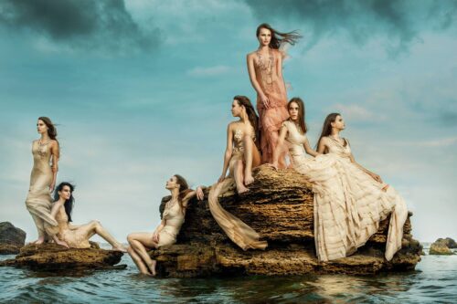 Des mannequins posent élégamment sur des rochers, vêtus de longues robes fluides dans des tons naturels, évoquant une esthétique sophistiquée et poétique, inspirée par la nature.